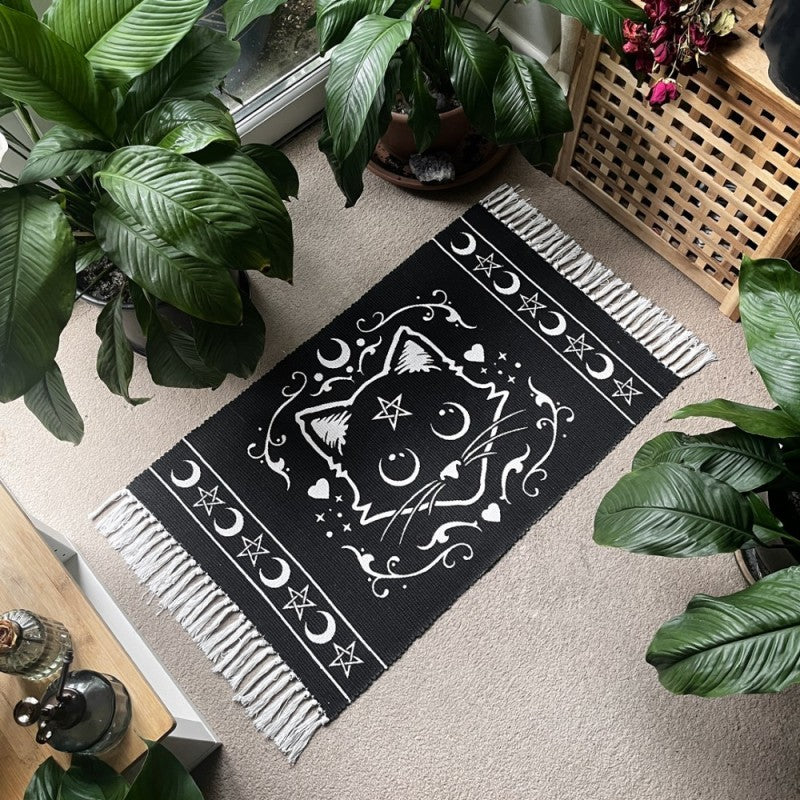 Black rug with white tassels with mystical white cat motif featuring pentagram stars and moons in a lifestyle setting
