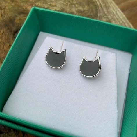 A pair of silver cat-shaped stud earrings with black enamel inlays, presented in a green jewelry box with a white insert.