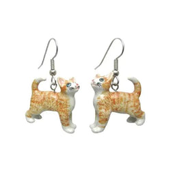 A pair of porcelain earrings shaped like ginger cats with white paws and blue eyes, attached to surgical steel hooks