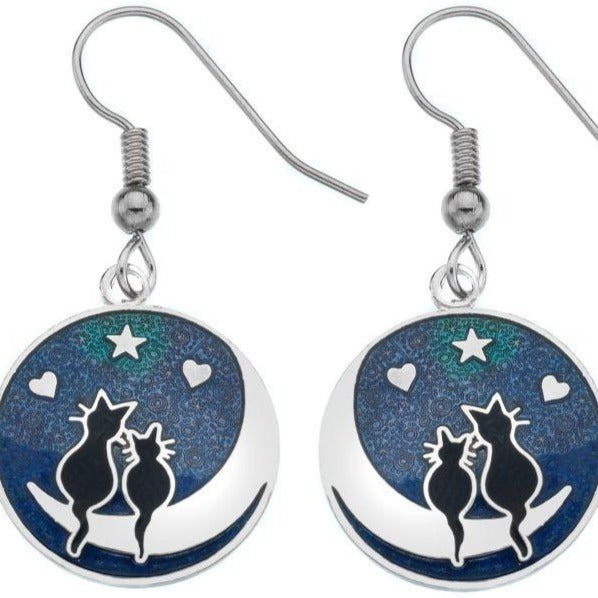 A pair of silver-coloured enamel earrings featuring a cat silhouette with a moon and stars design on a blue background